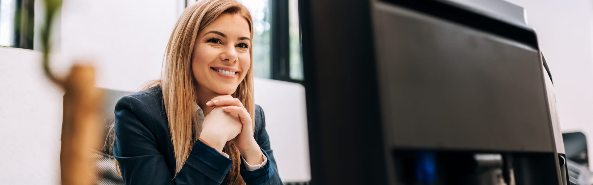Sucessful smiling businesswoman sitting at the office in front of a computer.
